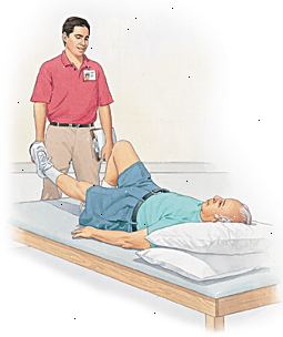 El hombre tumbado en la mesa con la cabeza apoyada en las almohadas, levantando una pierna. Proveedor de atención médica de pie junto a la mesa.