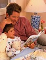 Fotografía de un padre que escucha a su hijo leer un libro antes de dormir Fotografía de un padre que escucha a su hijo leer un libro antes de dormir